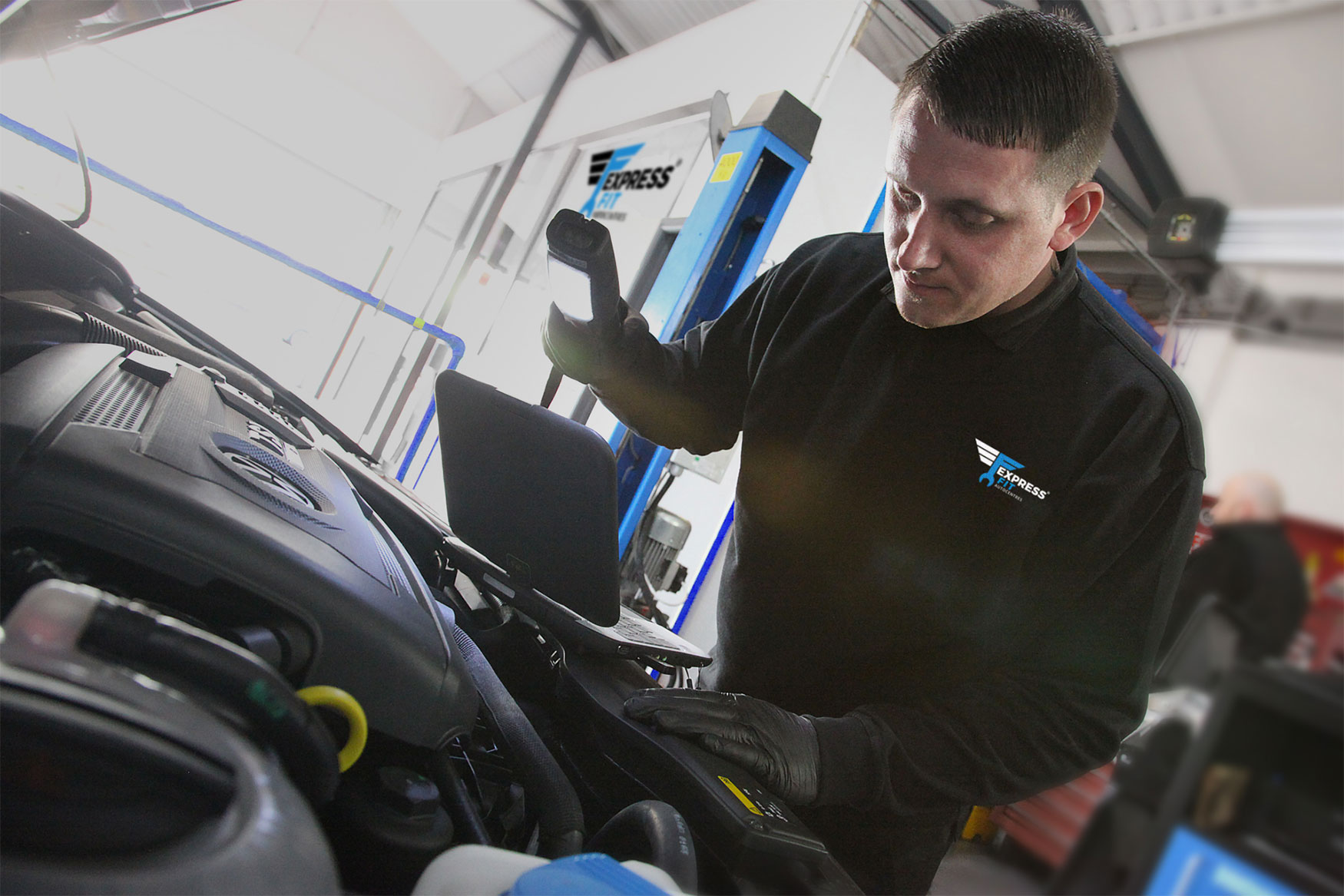 Mechanic with torch and laptop in car bonnet